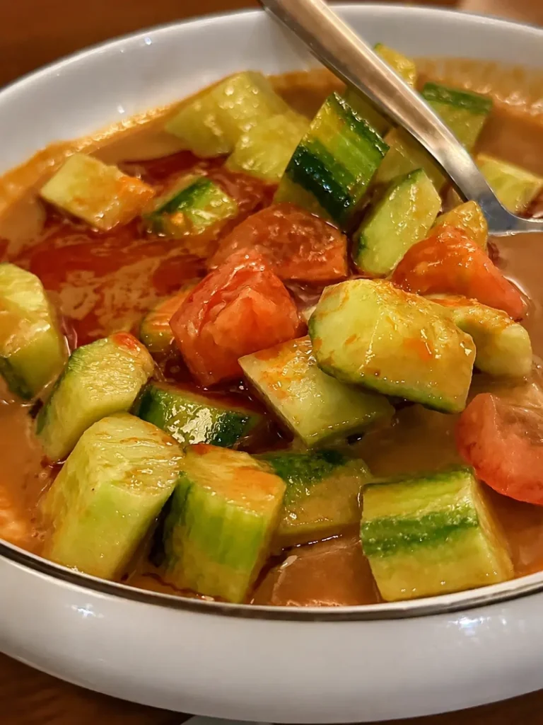 Tofu London vegan cucumber salad with fresh tomato, spicy dressing, and glossy chopped vegetables served in a white bowl.
