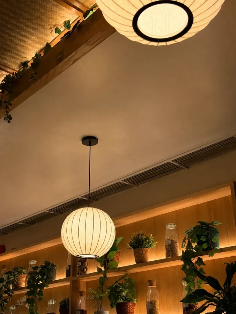 Tofu London restaurant interior with warm paper lantern lighting, wooden shelving, trailing plants, and a cozy modern Asian-inspired atmosphere.
