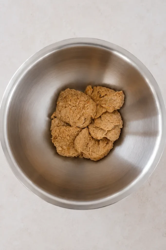 Vegan schnitzel soy chunks seasoned with spices in a stainless steel mixing bowl before breading.