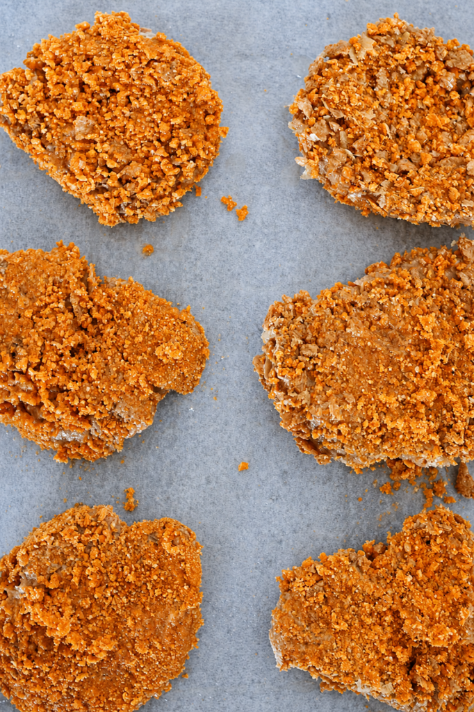 Vegan schnitzel pieces coated in a crunchy orange breadcrumb mixture and arranged on parchment paper before baking.