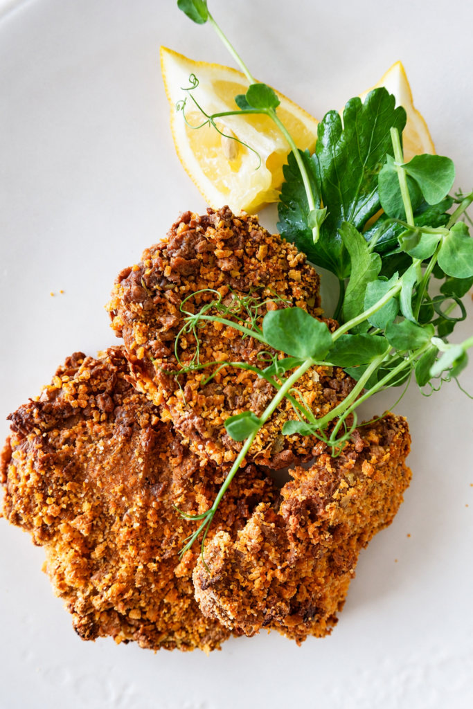 Vegan schnitzel with a crispy golden crust, served with lemon and fresh herbs in a close-up food photo.