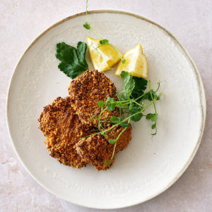 Vegan schnitzel served with lemon wedges, fresh parsley, and pea shoots on a pale ceramic plate.