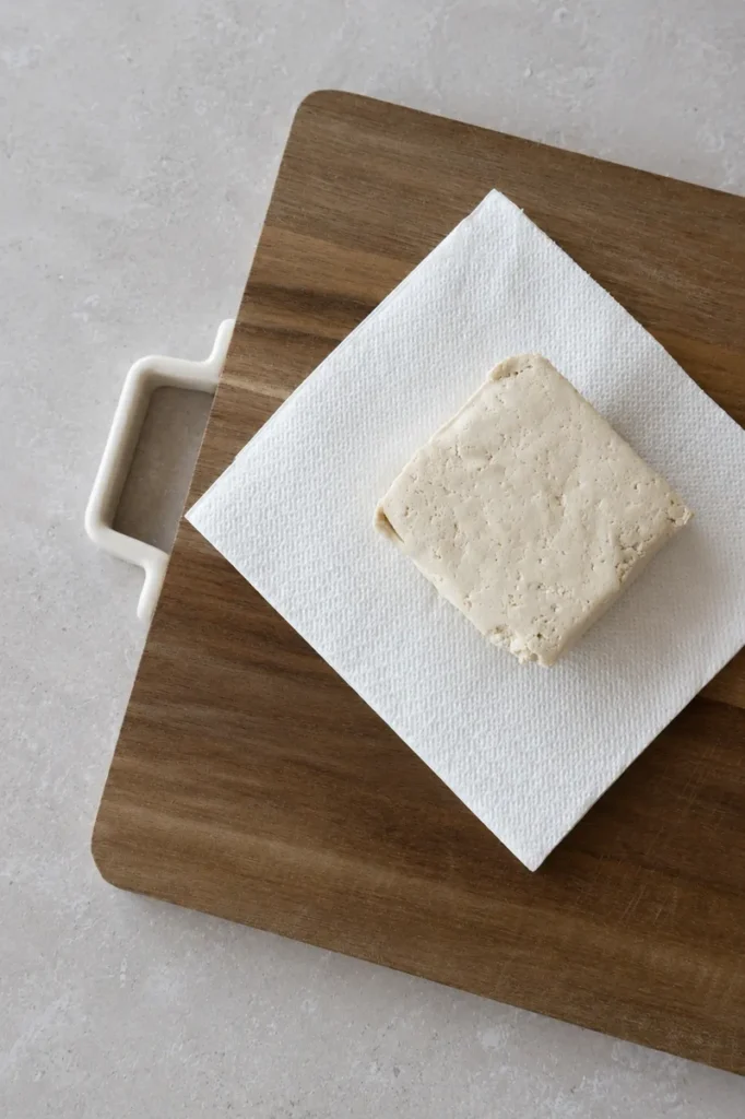vegan tofu scramble tofu block draining on paper towel over a wooden board before cooking