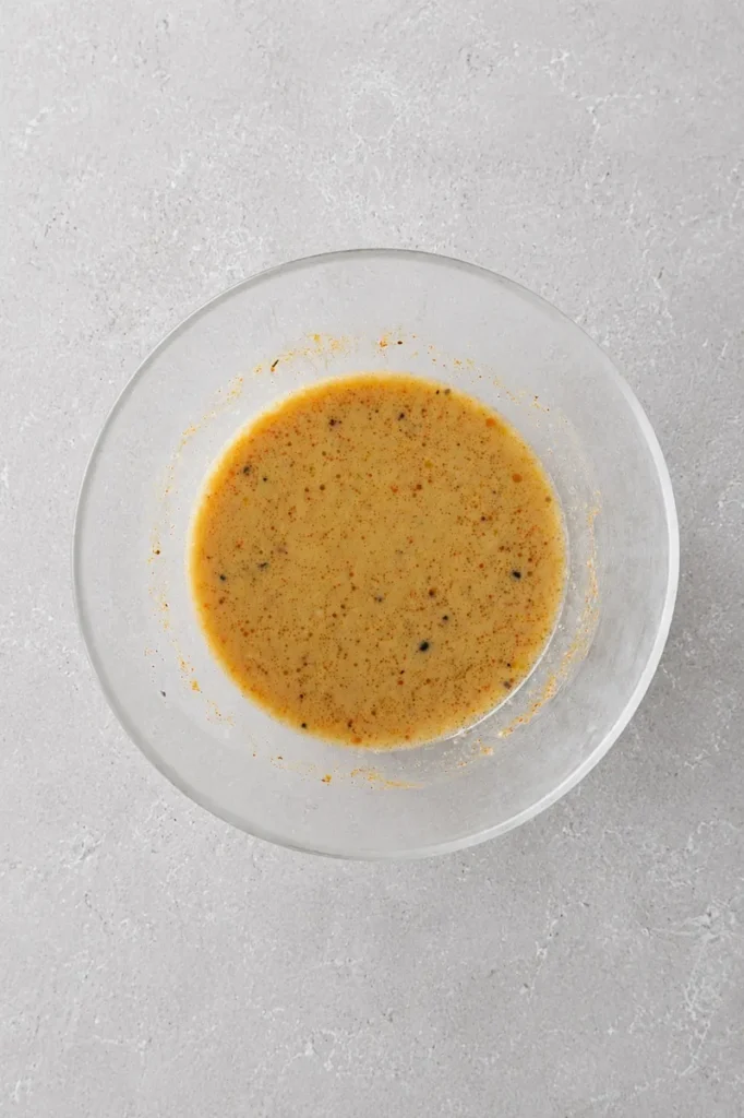 vegan tofu scramble seasoning mixture with plant milk, kala namak, mustard, and nutritional yeast in a clear bowl