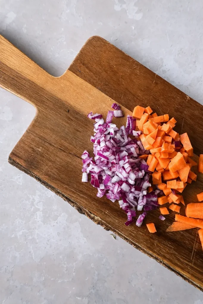 Split pea soup recipe prep with peeled potato and diced potato cubes on a rustic wooden board over a light stone surface.