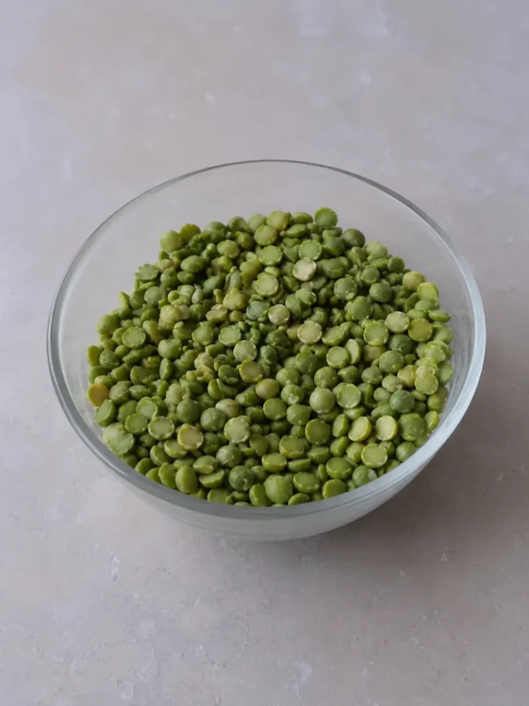 Split pea soup recipe ingredient close-up with dried green split peas in a glass bowl on a neutral stone surface.