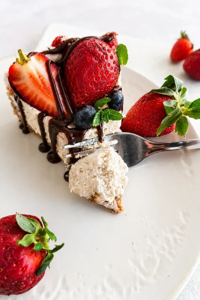 Vegan strawberry cheesecake topped with fresh strawberries, blueberries, mint and chocolate sauce on a light neutral background.
