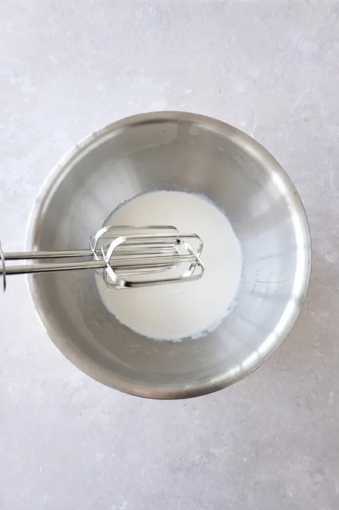 Vegan strawberry cheesecake vegan cream in a mixing bowl with electric beaters before whipping.