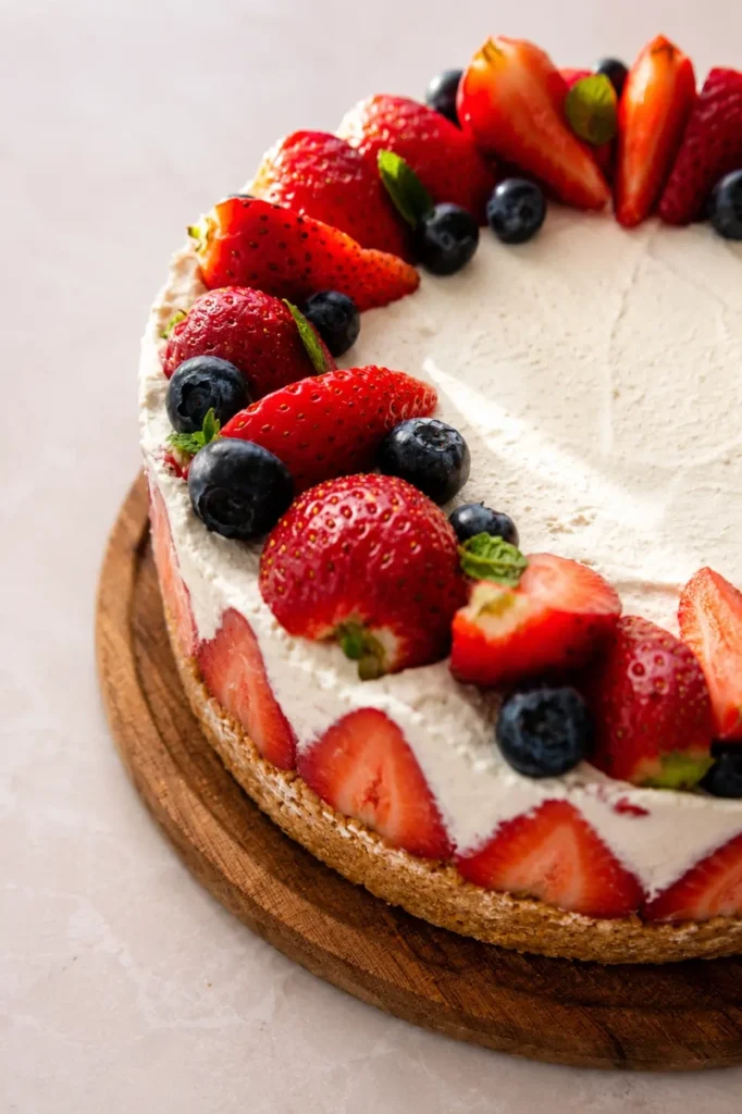 Vegan strawberry cheesecake topped with fresh strawberries, blueberries, and mint on a light background.