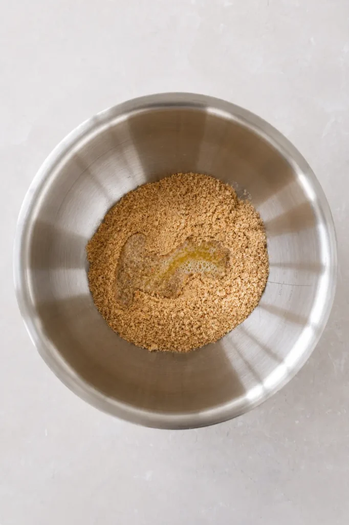 Vegan strawberry cheesecake crust mixture in a metal bowl with melted vegan butter added.