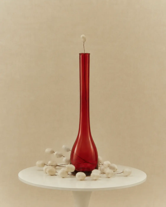 Is silk vegan article image with a red glass vase surrounded by white silkworm cocoons on a minimalist table against a warm beige backdrop.