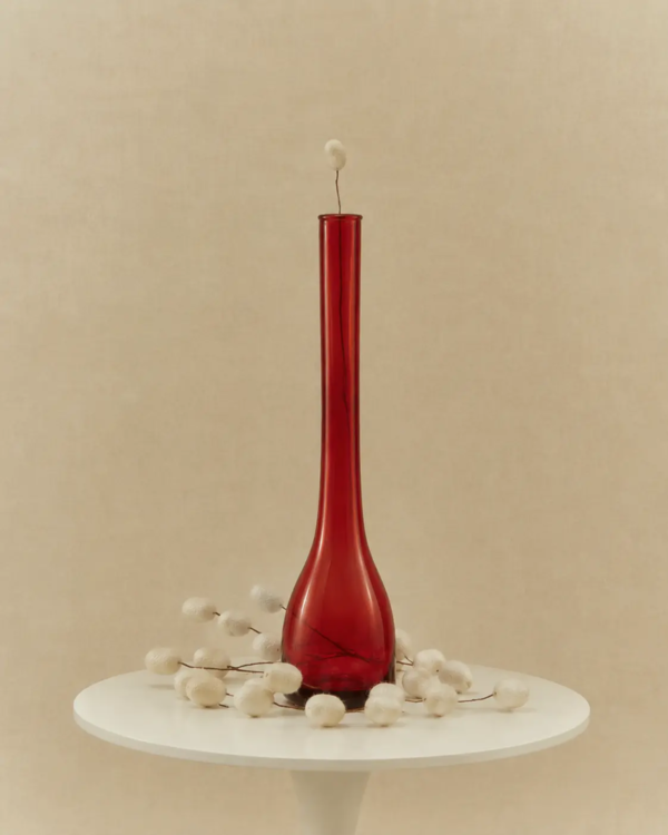 Is silk vegan article image with a red glass vase surrounded by white silkworm cocoons on a minimalist table against a warm beige backdrop.