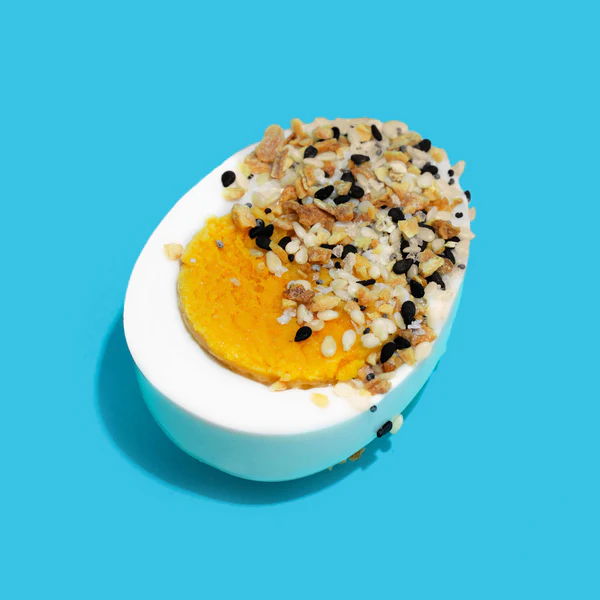 Vegan hard boiled egg substitute — WunderEggs plant-based egg half topped with black salt and seed garnish on white plate