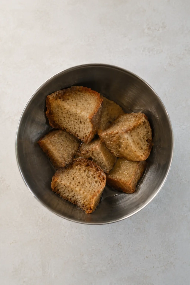 Vegan gazpacho bread soaked with vinegar in a stainless steel bowl on a light neutral surface