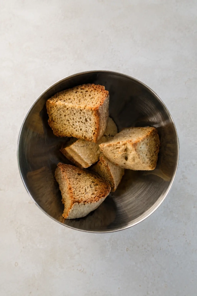 Vegan gazpacho stale bread cut into chunks in a stainless steel bowl on a light neutral surface