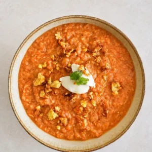 Vegan gazpacho served in a ceramic bowl with crispy tofu, creamy vegan garnish, fresh mint, and olive oil on a textured neutral surface