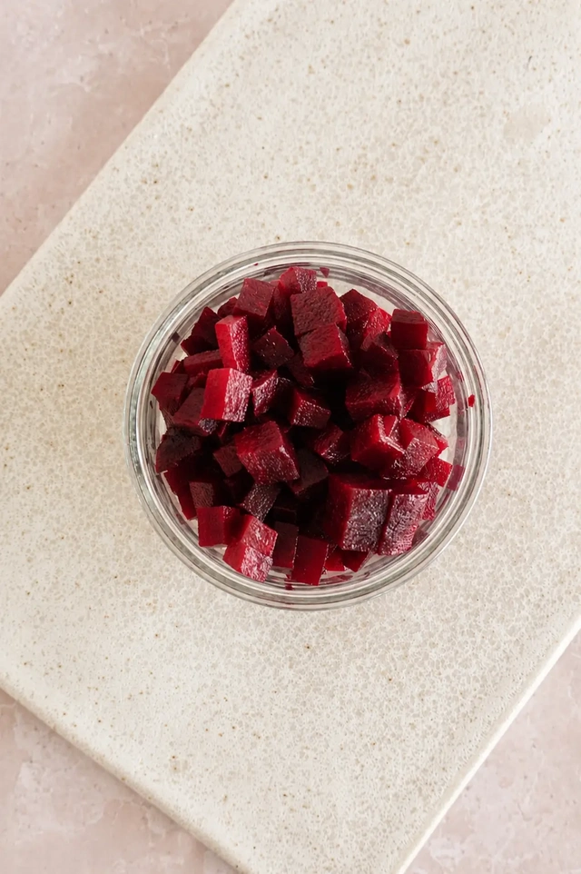Diced beetroot in a glass bowl on a pale cutting board, prepared as an ingredient for a fresh vegan bean salad.