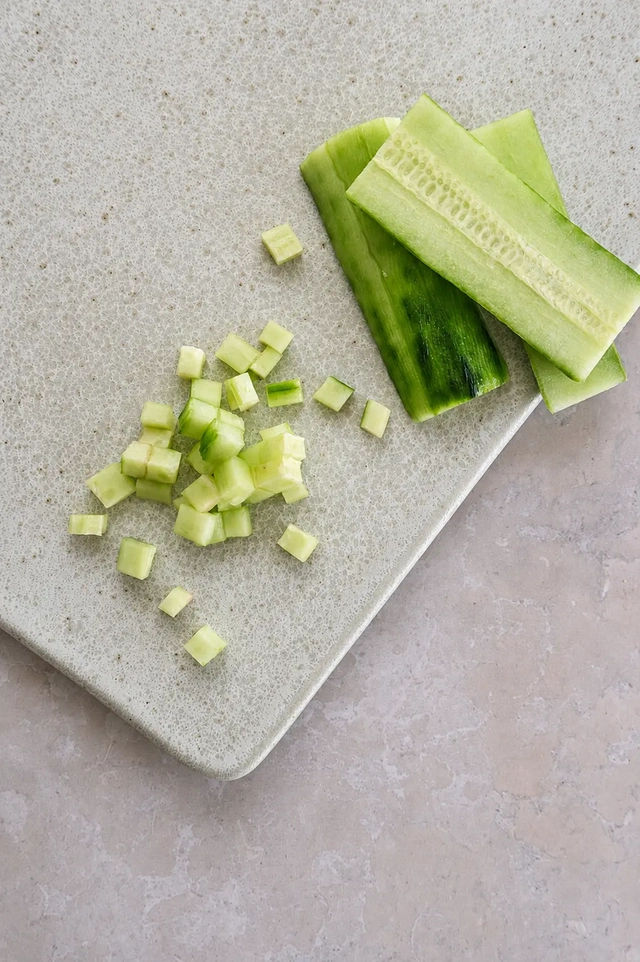 Fresh cucumber slices and diced cucumber on a pale cutting board, prepared for a crunchy vegan bean salad.