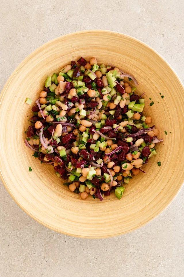 Finished vegan bean salad with mixed beans, cucumber, beetroot, red onion, avocado, and herbs in a natural bamboo bowl.