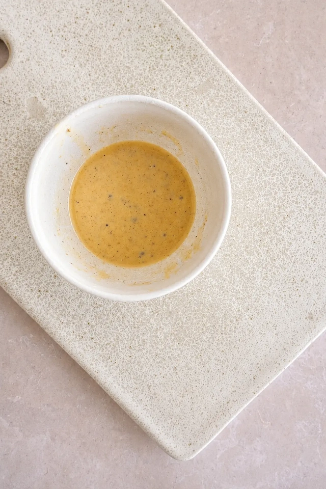 Creamy tahini dressing in a white bowl on a pale cutting board, prepared for a fresh vegan bean salad.