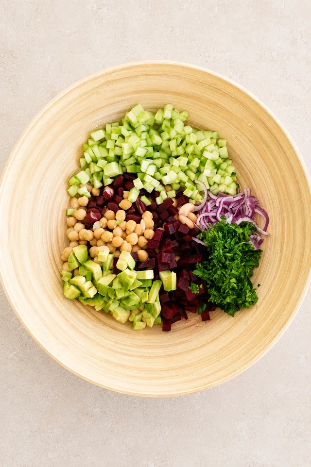 Fresh vegan bean salad with chickpeas, beans, cucumber, beetroot, red onion, avocado, and parsley in a bamboo bowl.
