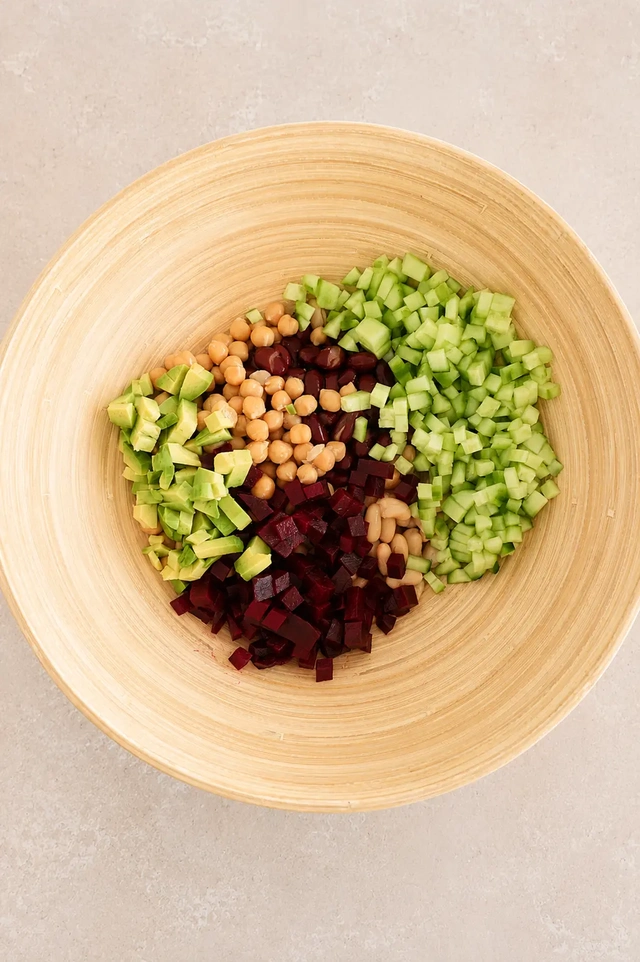 Vegan bean salad ingredients arranged in a bamboo bowl with chickpeas, beans, cucumber, avocado, beetroot, and herbs.