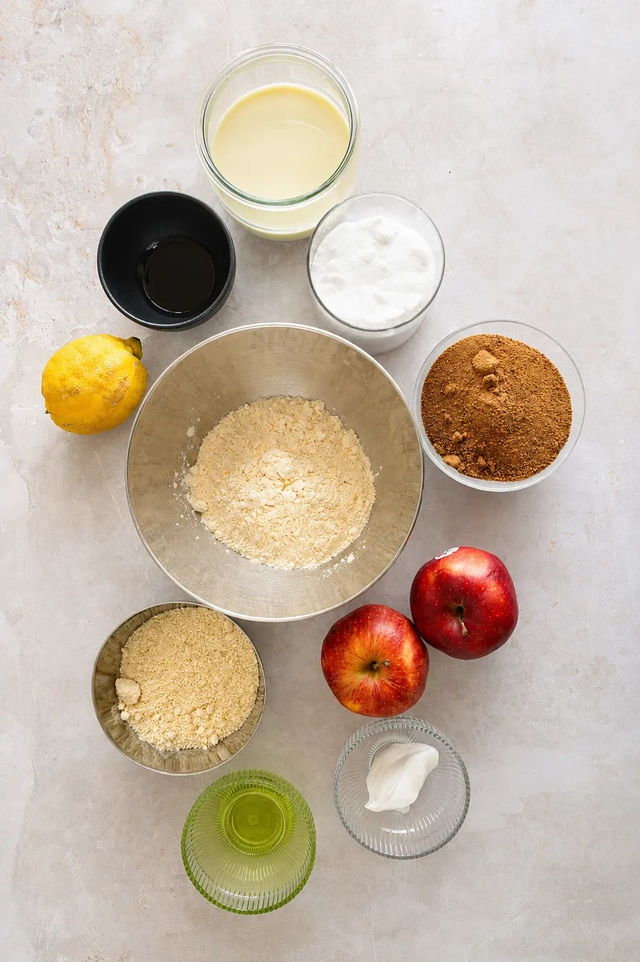 Ingredients for vegan egg substitutes arranged in a flat lay, including almond flour, plant milk, oil, sugar, apples, lemon, and yogurt, for a guide on replacing eggs in recipes.
