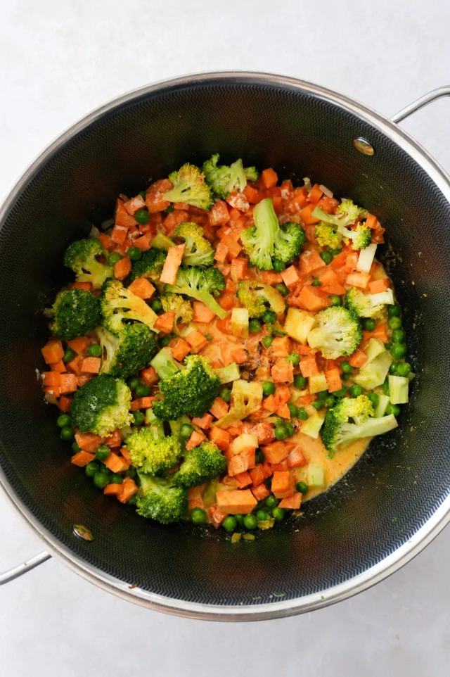 Vegan korma vegetables sautéing in a large pot with broccoli, carrots, peas and creamy spiced sauce.