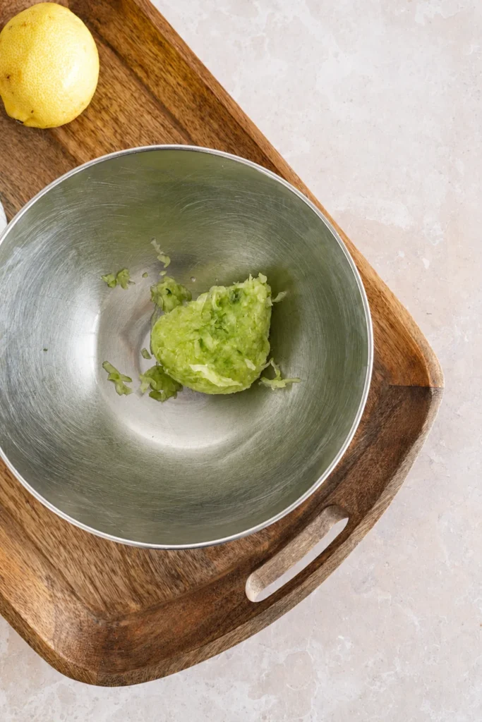 Vegan tzatziki sauce recipe step showing squeezed grated cucumber in a stainless steel bowl after removing the excess liquid.