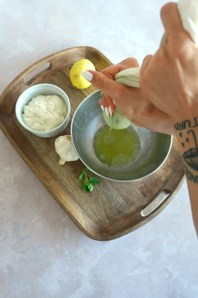 Vegan tzatziki sauce recipe step showing grated cucumber being squeezed by hand over a bowl to remove liquid and keep the sauce creamy.