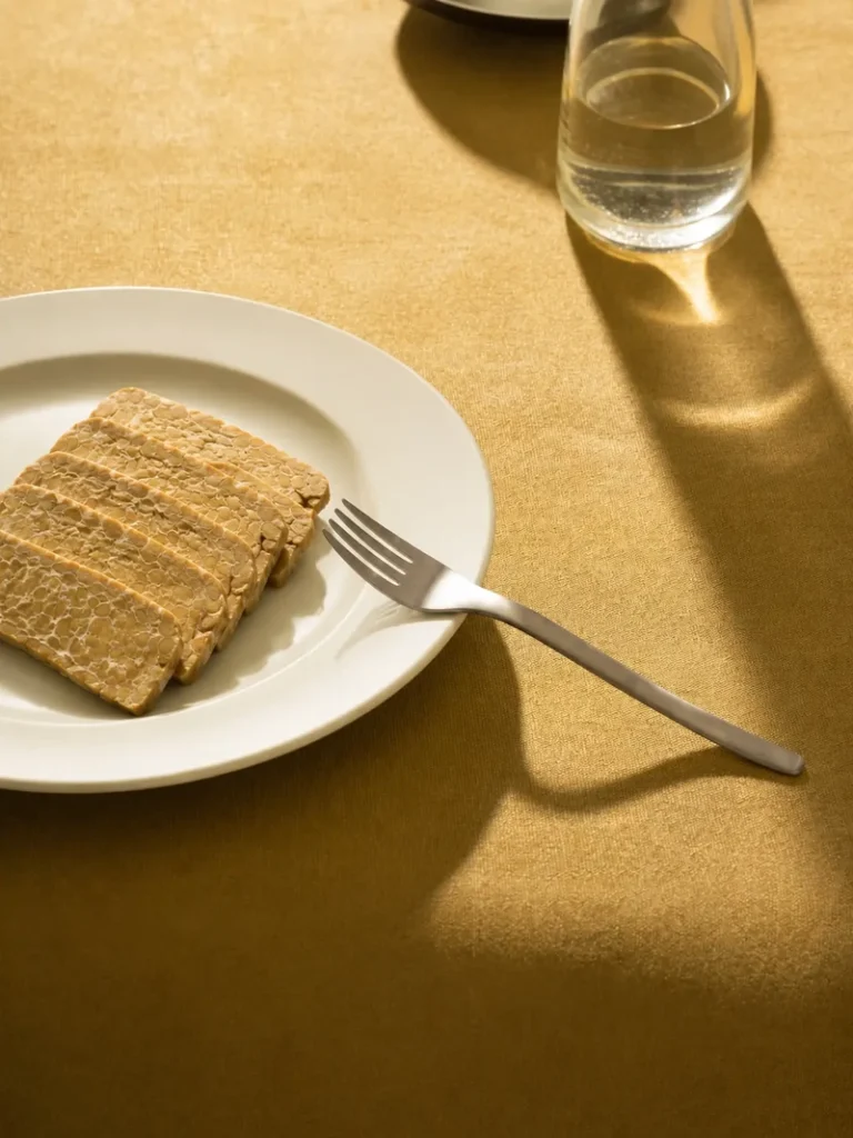 Tempeh cut in half on a rustic wooden board, photographed in warm natural light against a textured beige background.