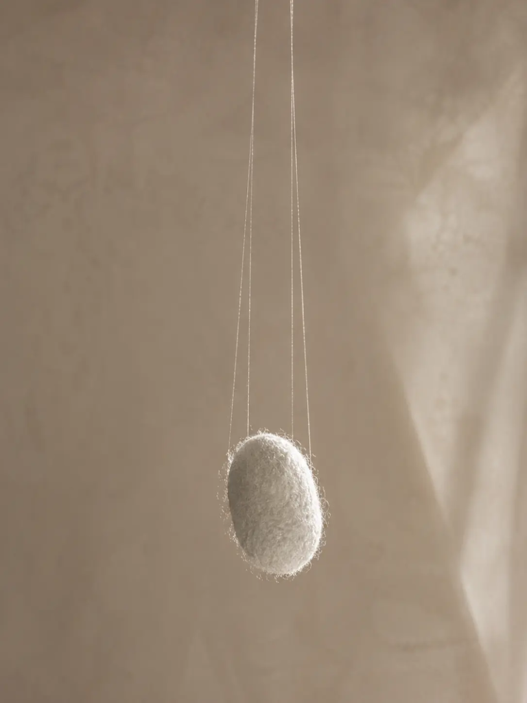 Is silk vegan article image with a suspended white silkworm cocoon hanging from delicate silk threads against a soft neutral beige background.