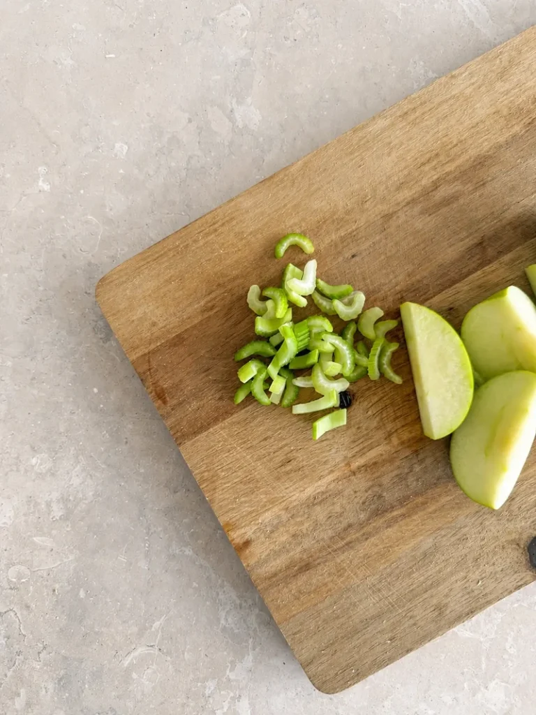 Vegan Waldorf Salad celery sliced into small diagonal pieces on a wooden cutting board beside green apple wedges.