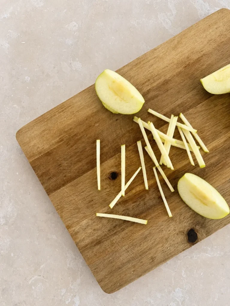 Vegan Waldorf Salad green apple cut into thin julienne-style matchsticks on a wooden cutting board.