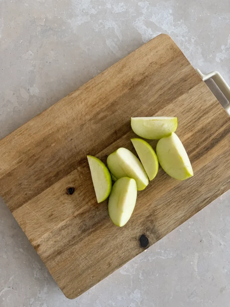 Vegan Waldorf Salad apple slices arranged on a wooden cutting board over a light stone surface, showing green apple wedges ready to be cut for the salad.