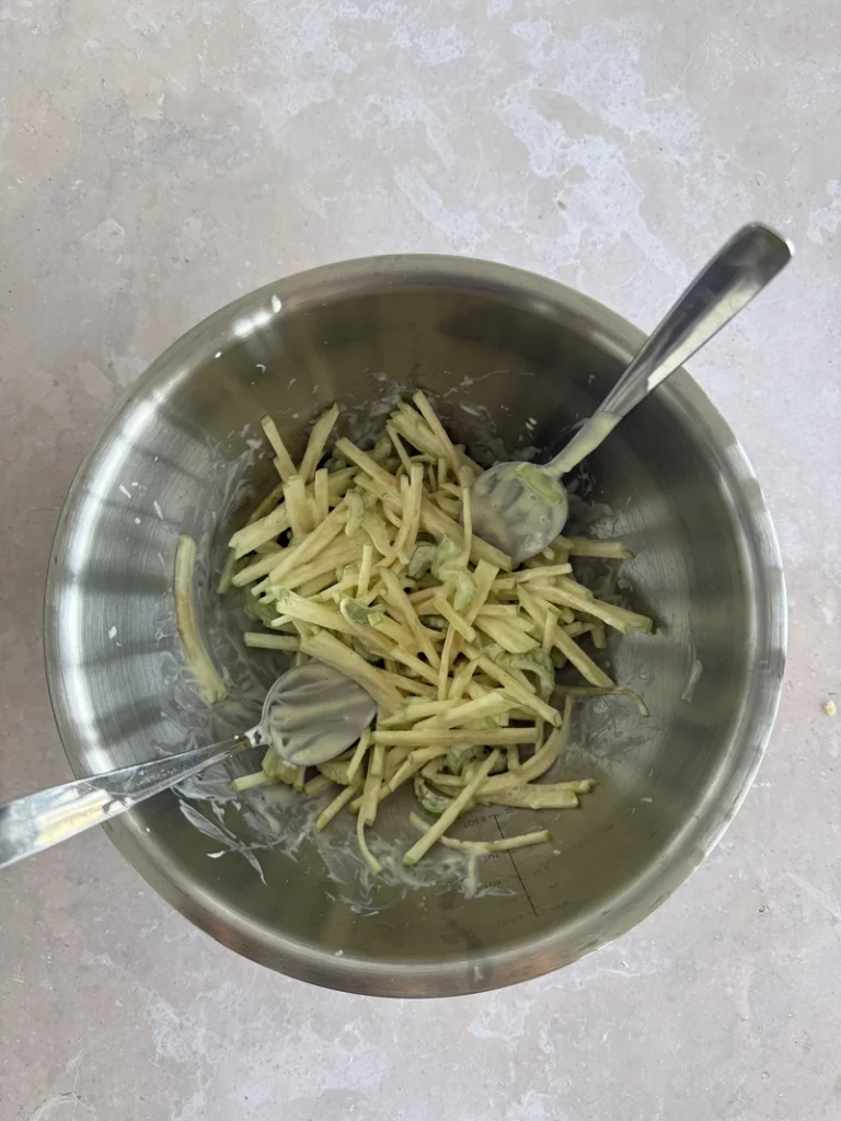 Vegan Waldorf Salad apple and celery coated in creamy vegan mayonnaise inside a stainless steel mixing bowl.