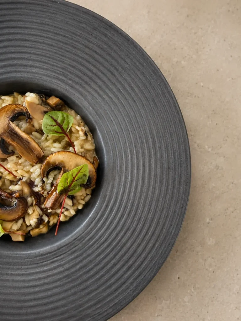 Vegan Mushroom Risotto on a black plate with mushrooms and green leaves - Inumami's newsletter