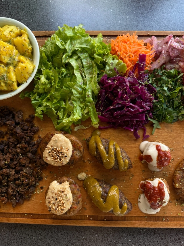 Eating vegan and gluten free with a colorful mezze-style platter of salads, roasted potatoes, plant-based patties, hummus, cabbage, carrots, and fresh herbs.