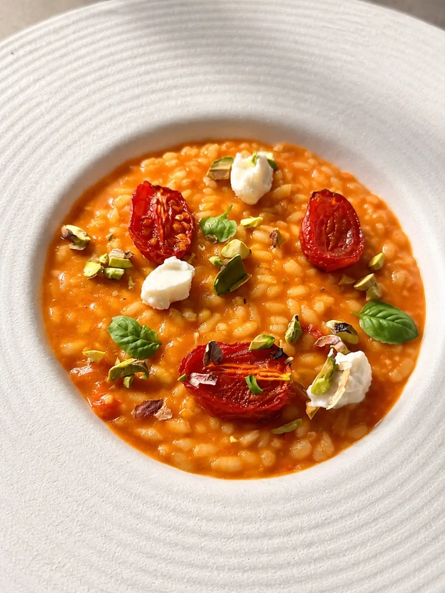 Eating vegan and gluten free with creamy tomato risotto topped with roasted cherry tomatoes, pistachios, basil, and plant-based cheese.