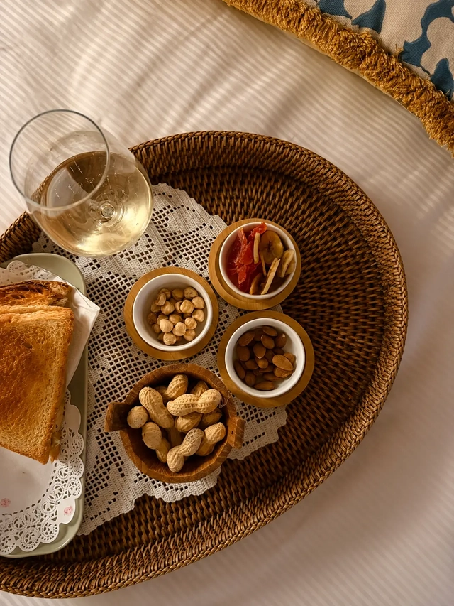 Vegan and gluten free diet snack tray with toasted bread, mixed nuts, dried fruit, peanuts, and a glass of white wine served on a woven tray.