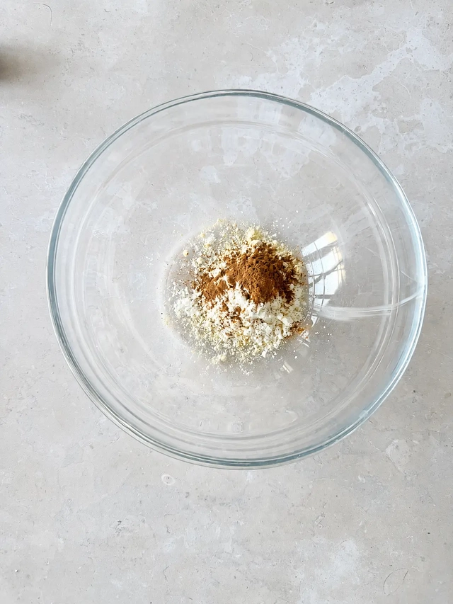 Dry ingredients for vegan French toast in a clear glass bowl, including chickpea flour, cornstarch, and cinnamon, photographed from above.
