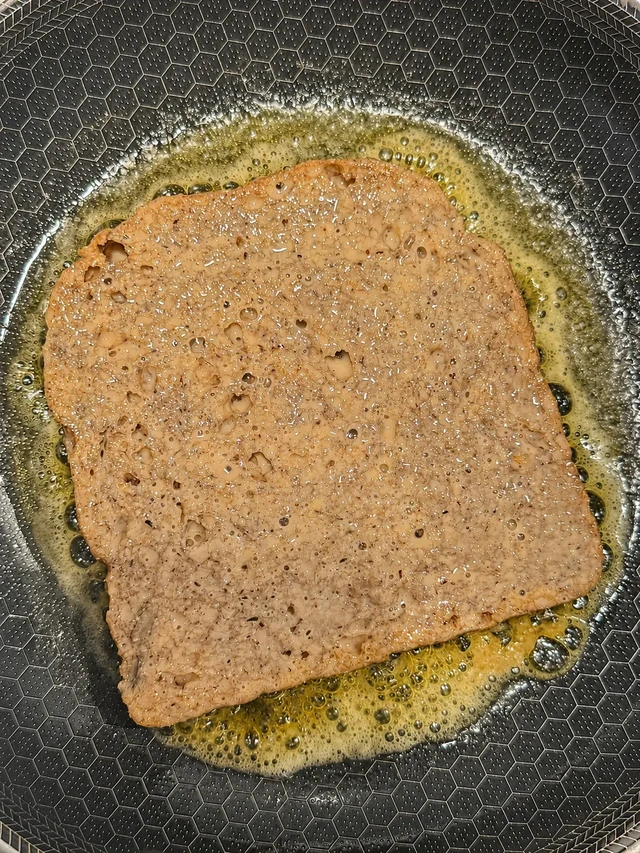 Vegan buckwheat French toast cooking in vegan butter in a non-stick frying pan, photographed from above.