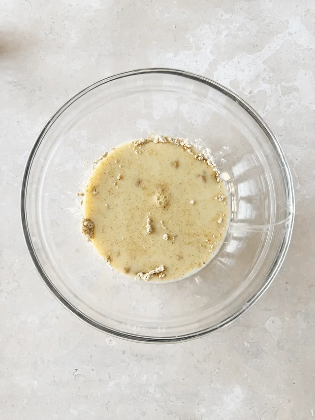 Vegan French toast batter in a clear glass bowl, made with plant-based milk, chickpea flour, cornstarch, vanilla, and cinnamon, photographed from above.