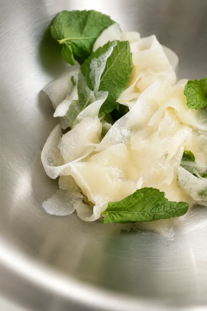 Cantaloupe salad preparation with shaved melon and mint leaves viewed from above