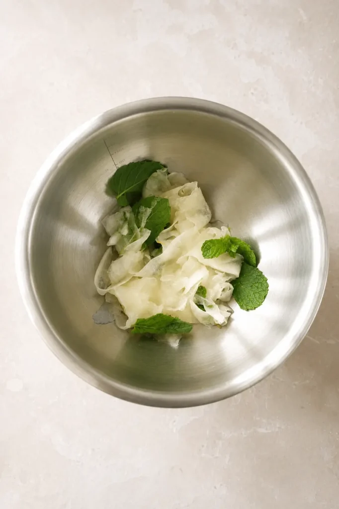 Cantaloupe salad with thin melon ribbons and fresh mint in a stainless steel bowl