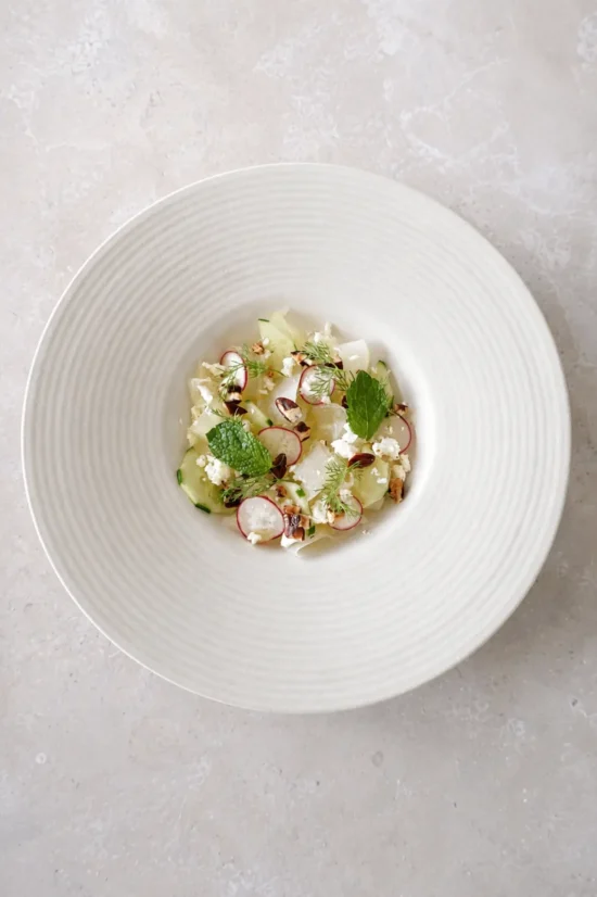 Honeydew cucumber salad with lime-marinated melon, vegan feta, radishes, pecans, mint, and fresh dill served on a white ceramic plate.