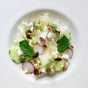 Honeydew cucumber salad close up with lime-marinated melon, vegan feta, radishes, pecans, mint, and fresh dill served on a white ceramic plate.