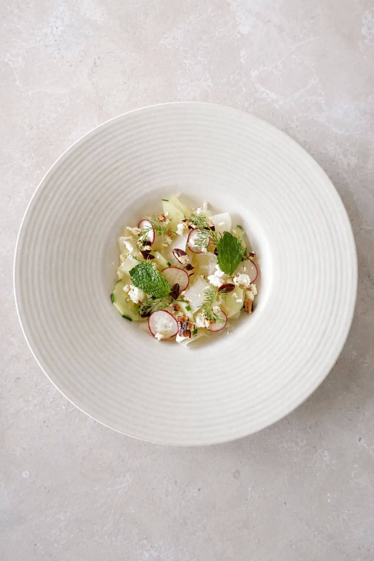 Honeydew cucumber salad with lime-marinated melon, vegan feta, radishes, pecans, mint, and fresh dill served on a white ceramic plate.