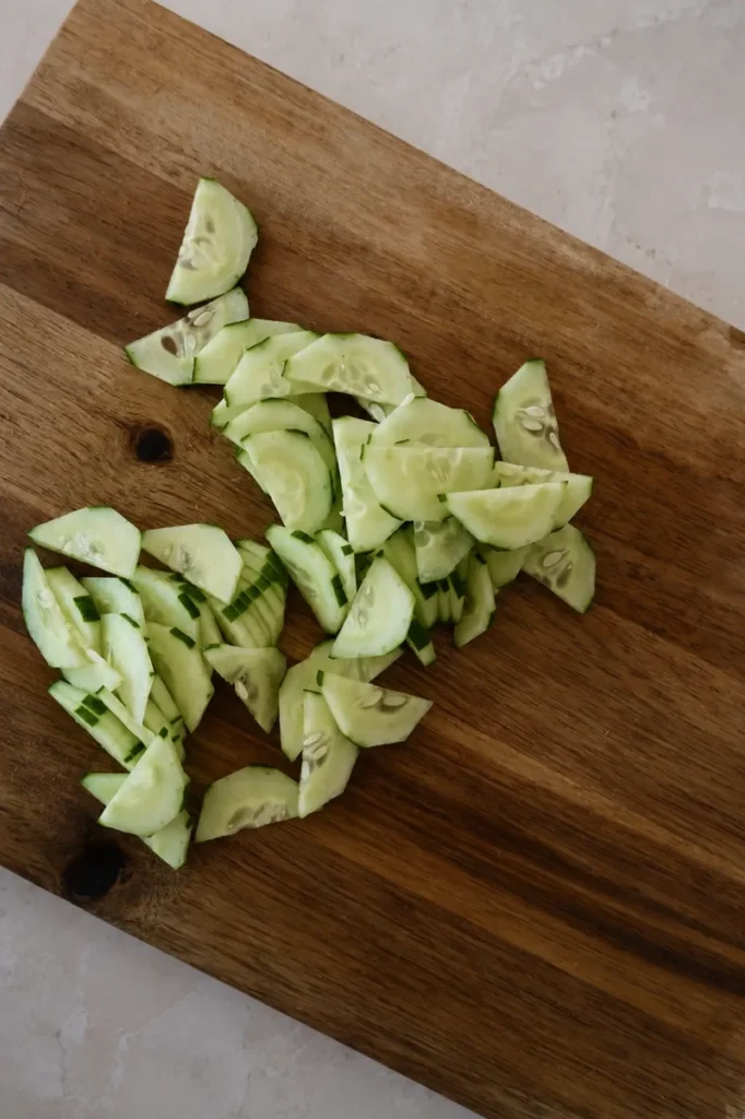 Sliced cucumber on a wooden cutting board during salad preparation
