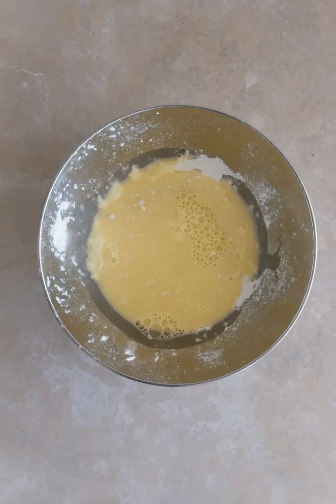 Overhead view of a metal mixing bowl with the wet ingredients for a vegan tart crust, partially mixed on a light stone surface.